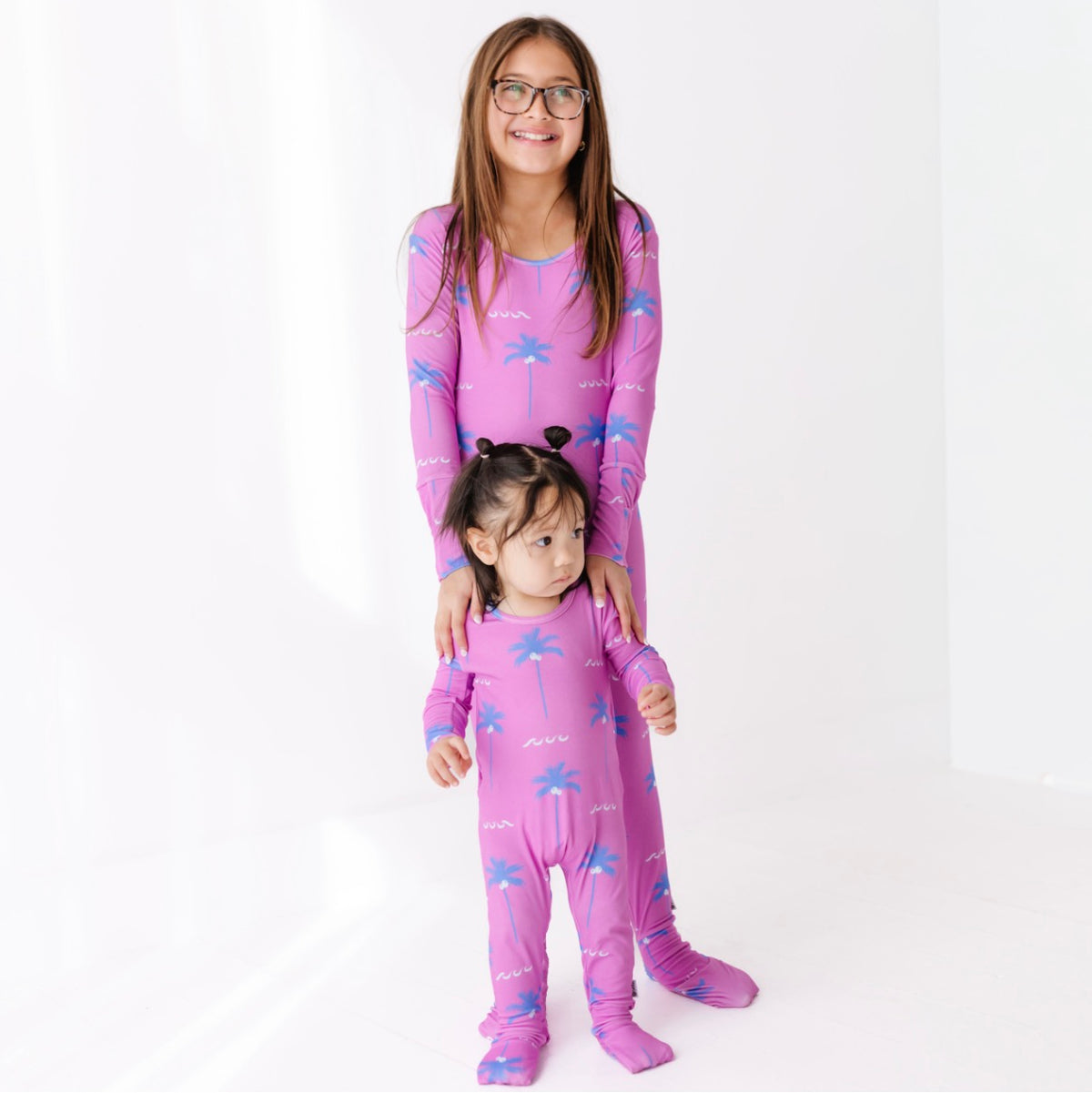 Two children wearing matching pink pajamas with a white background