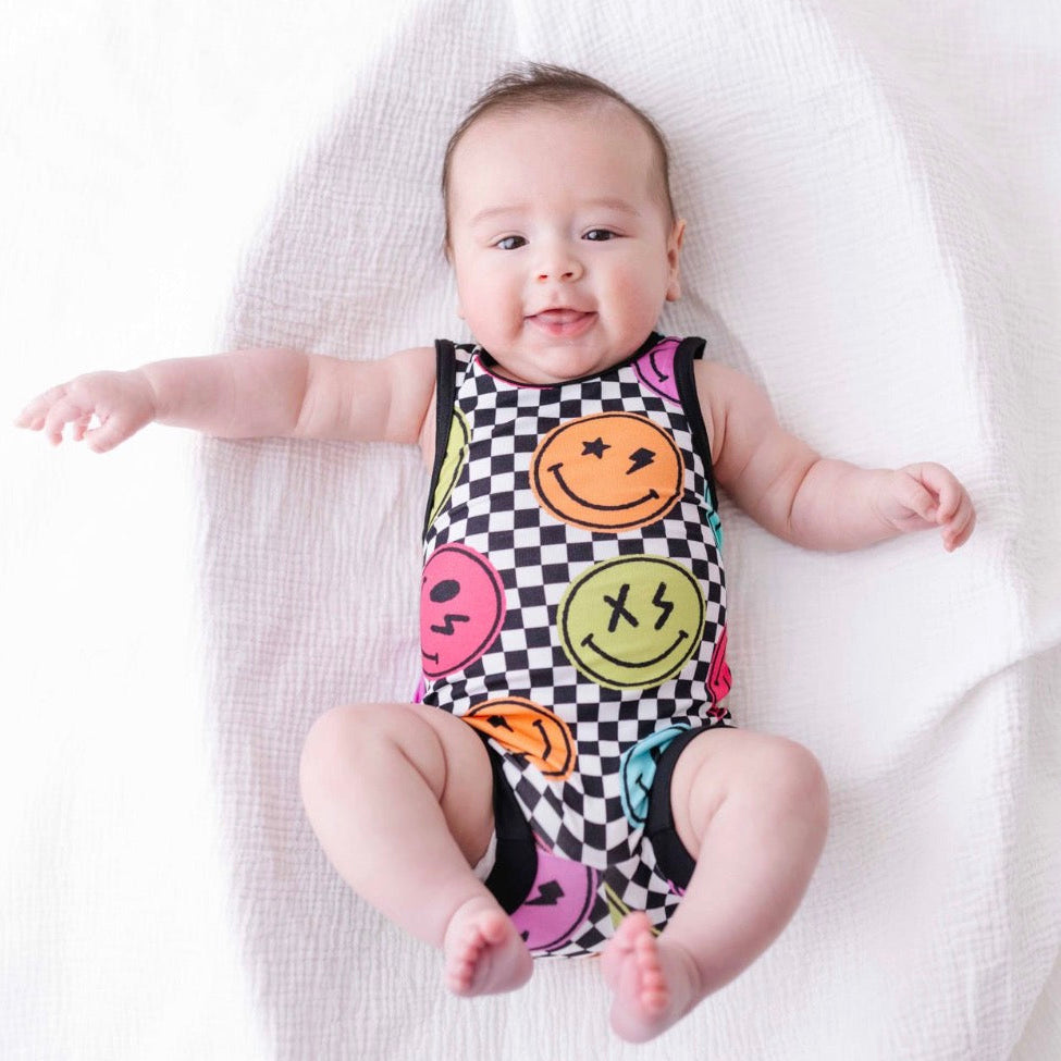Baby wearing a colorful onesie with smiley face patterns on a white blanket