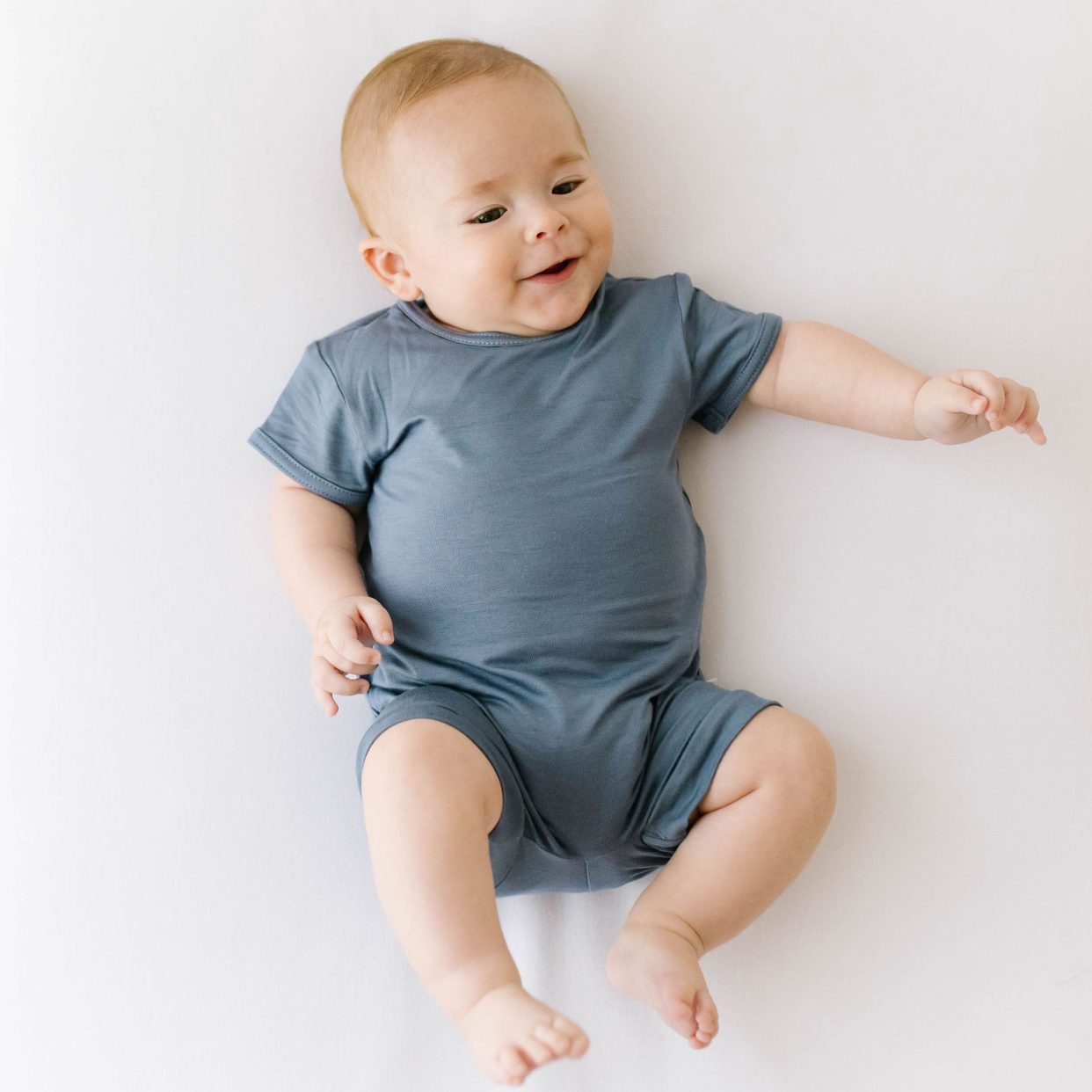 A smiling infant wearing a gray short-sleeved romper suit.
