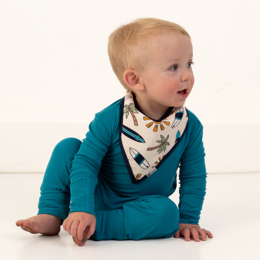 Baby wearing a blue onesie and a bandana with a nautical design on a white background