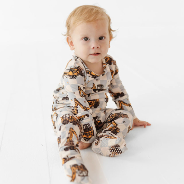Baby wearing a onesie with construction vehicle pattern on a white background