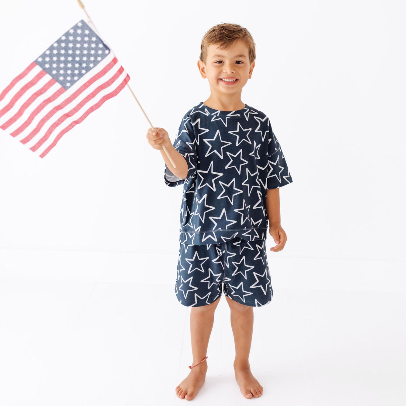 Child wearing a star-patterned outfit holding an American flag on a white background