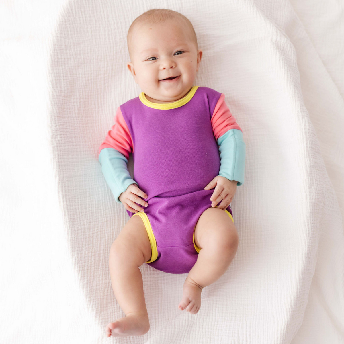 Baby wearing a colorful onesie on a white blanket