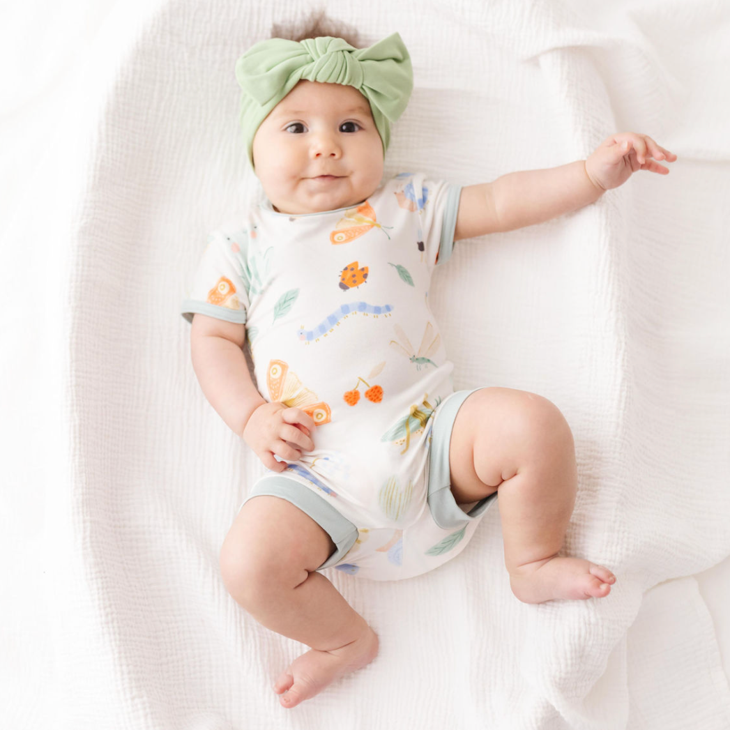 Baby lying on a white blanket wearing a floral onesie and green headband.