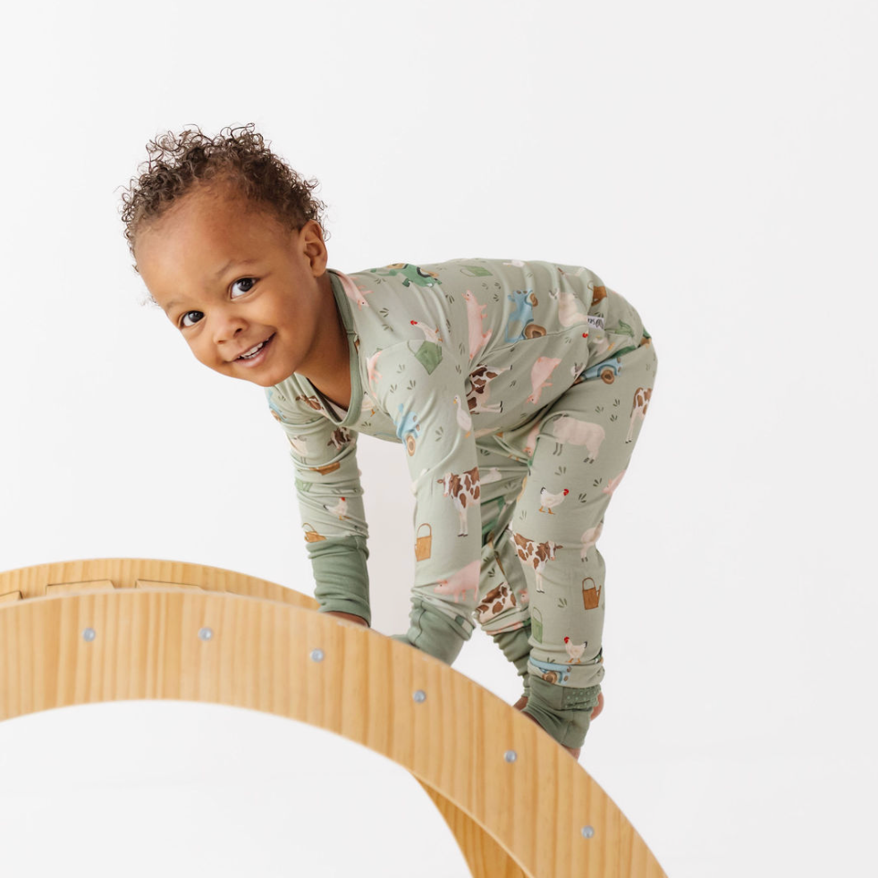 Child in patterned pajamas standing next to a wooden toy track on a white background