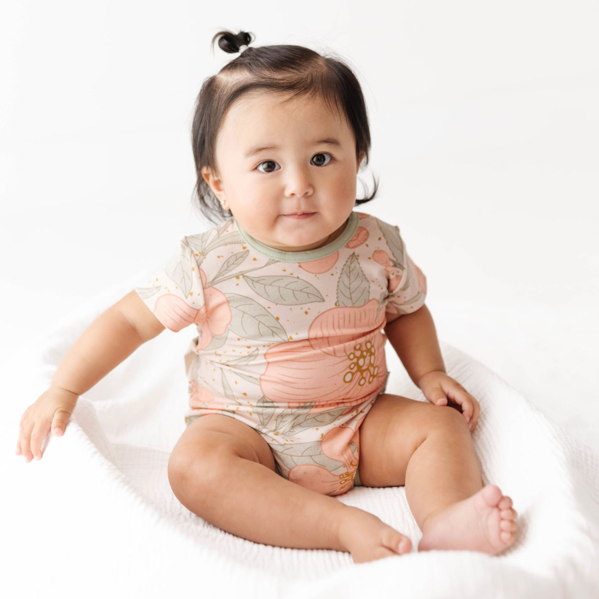 Baby wearing a floral onesie sitting on a white blanket