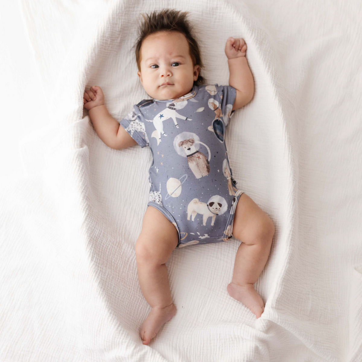Baby wearing a patterned onesie lying on a white blanket