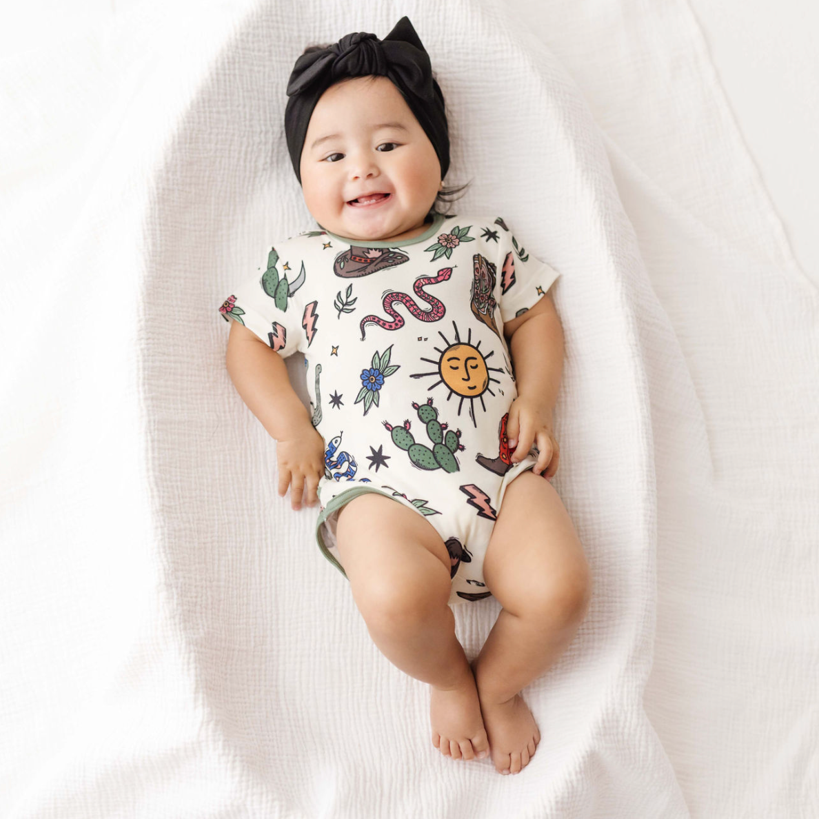 Baby wearing a onesie with nature-themed designs on a white blanket