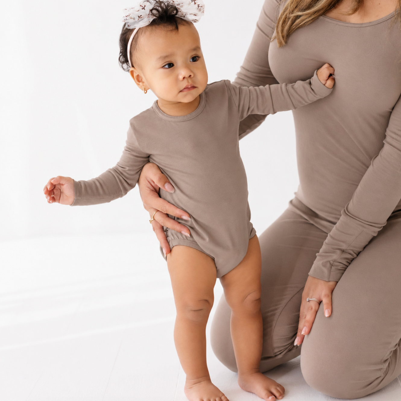 Woman in a brown outfit holding a baby in a matching outfit against a white background