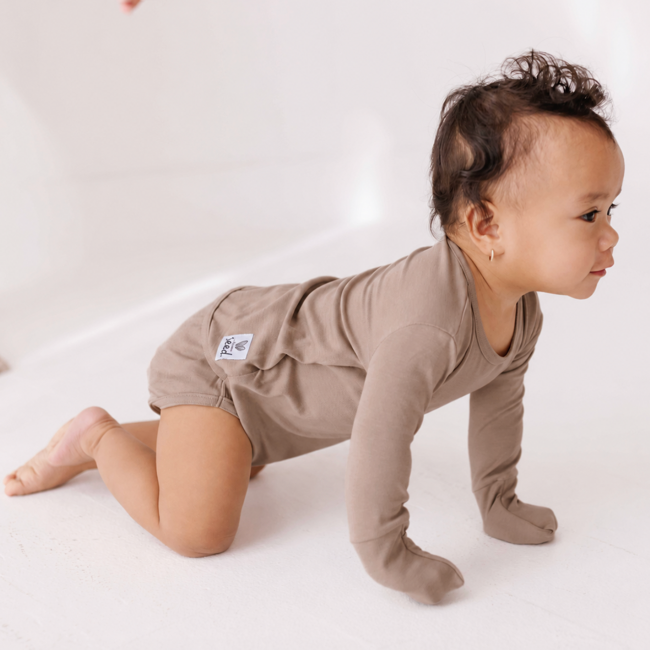 Baby in a beige onesie crawling on a white surface