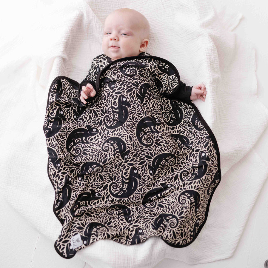 Baby wrapped in a black and white patterned swaddle on a white blanket