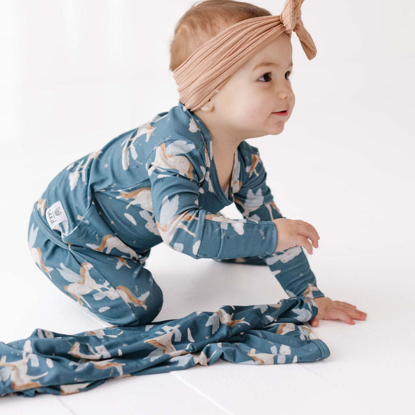 Baby in a blue patterned outfit and headband on a white background