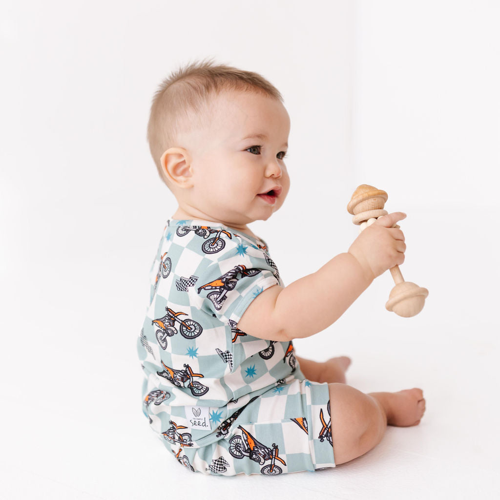 Baby wearing a patterned onesie holding a wooden toy on a white background