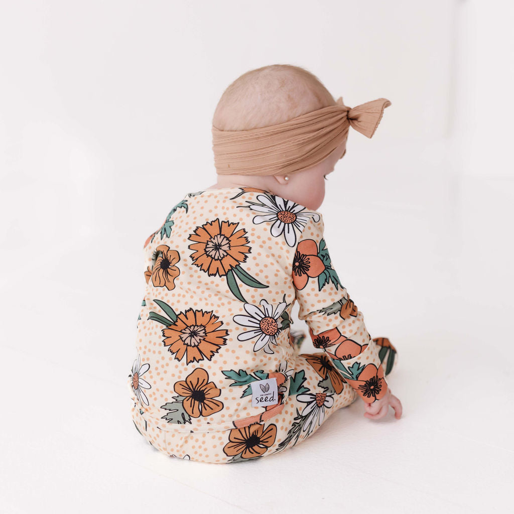 Baby wearing a floral onesie and turban on a white background