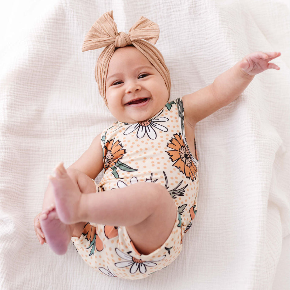 Baby wearing a floral romper and headband on a white blanket