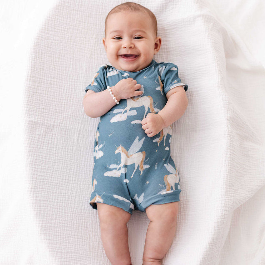 Baby wearing a blue romper with unicorn design on a white blanket
