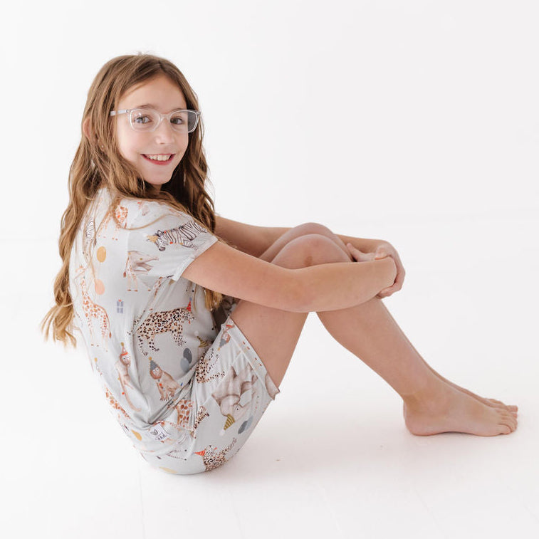 Young girl sitting on a white background wearing a patterned outfit.