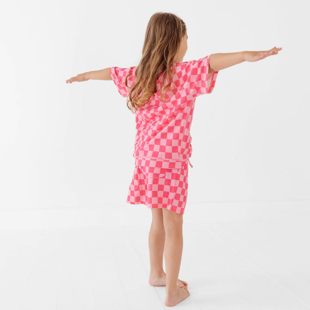 Child wearing a pink checkered dress standing with arms outstretched on a white background