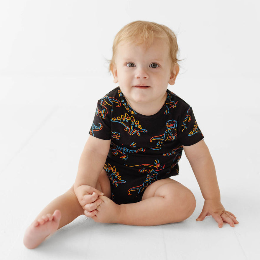 Baby wearing a black onesie with colorful dinosaur patterns on a white background