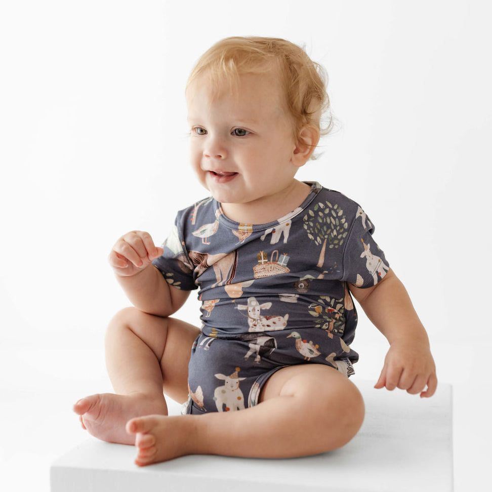 Baby wearing a patterned onesie sitting on a white surface