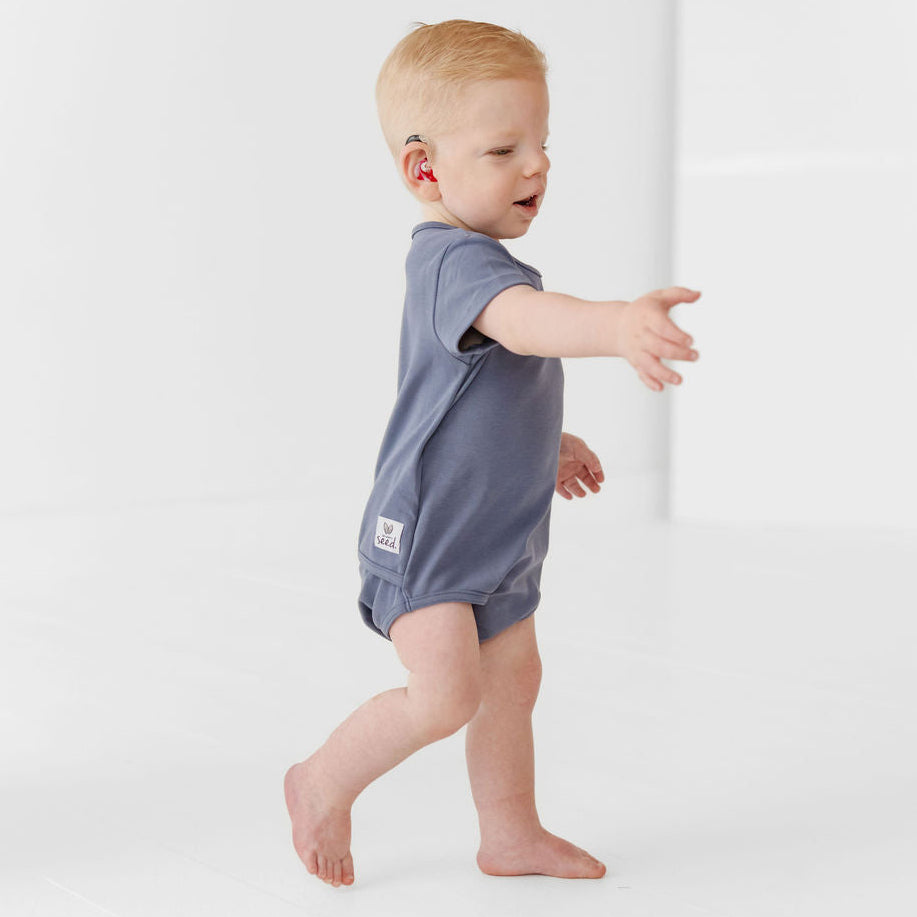 Baby in a blue onesie standing on a white background