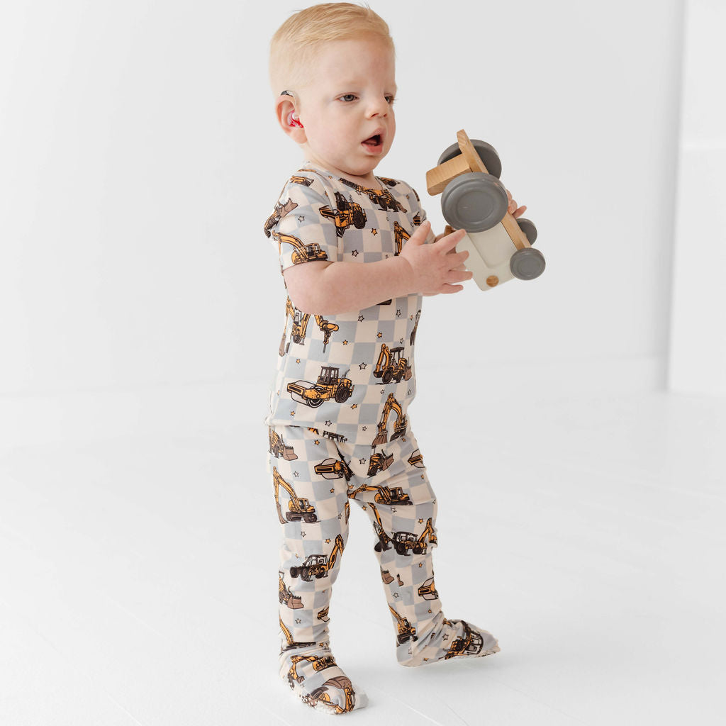 Child wearing a patterned onesie holding a toy on a white background