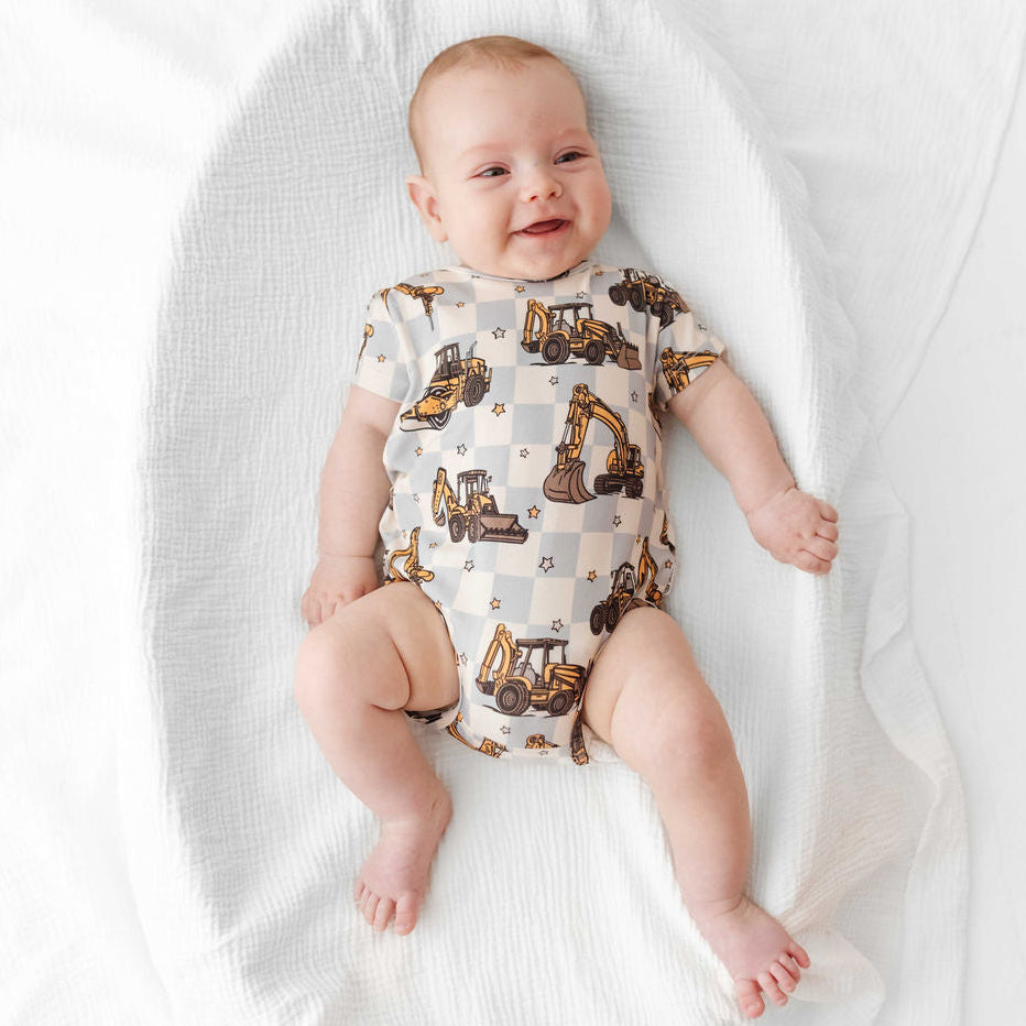 Baby wearing a onesie with construction vehicle pattern on a white blanket