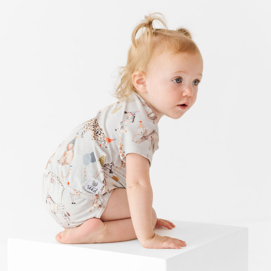 Baby in a patterned onesie sitting on a white surface with a plain background