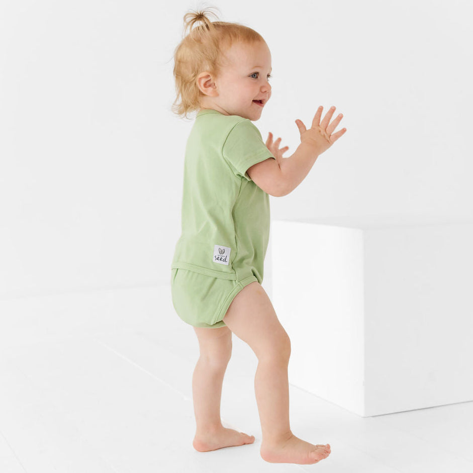 Baby in a green outfit standing on a white background