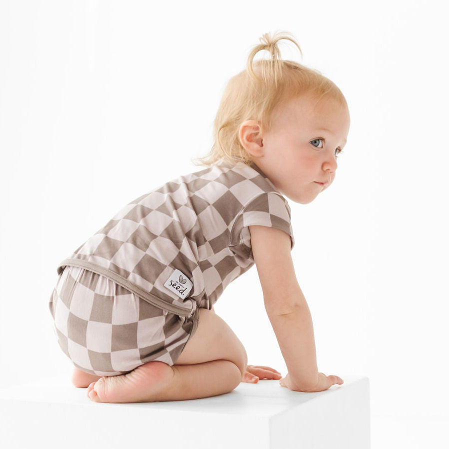 Baby in a checkered outfit sitting on a white surface