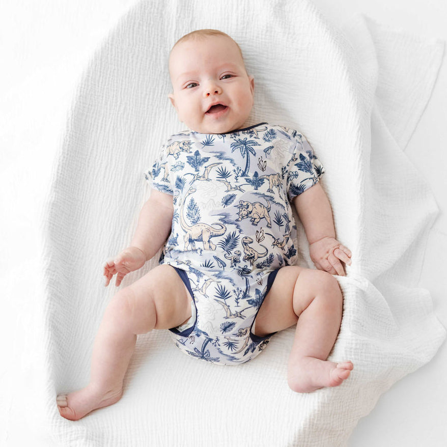 Baby wearing a blue and white patterned onesie lying on a white blanket