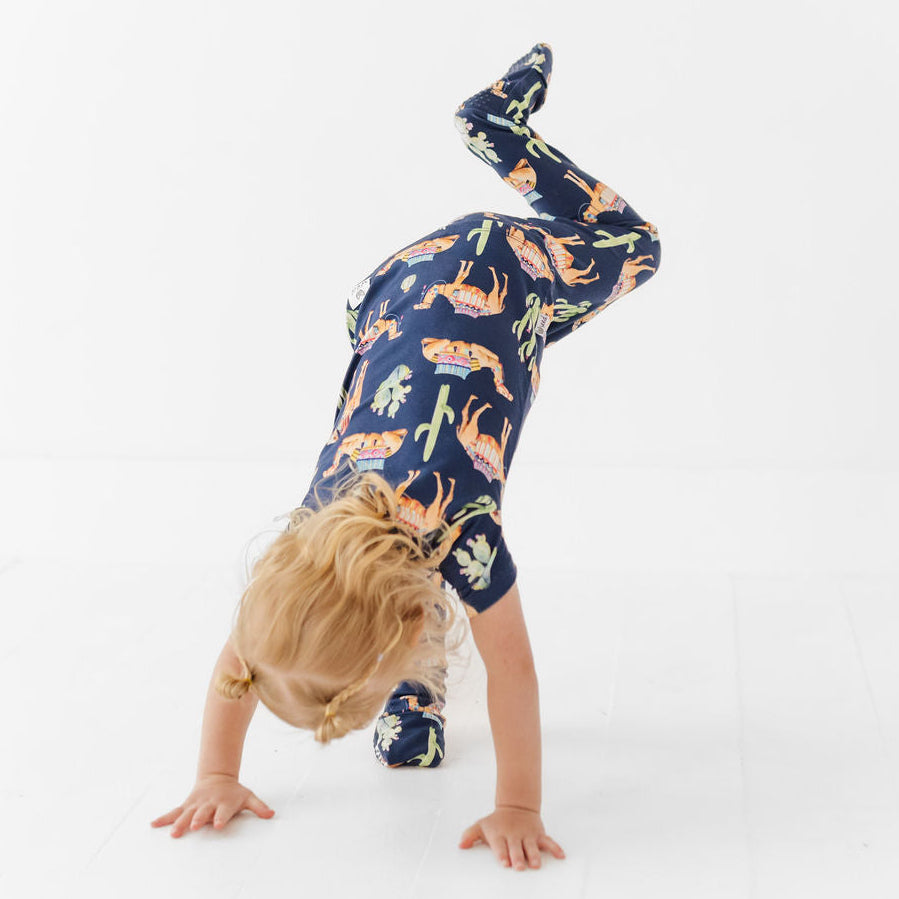 Child wearing a navy blue onesie with animal print, doing a handstand on a white background