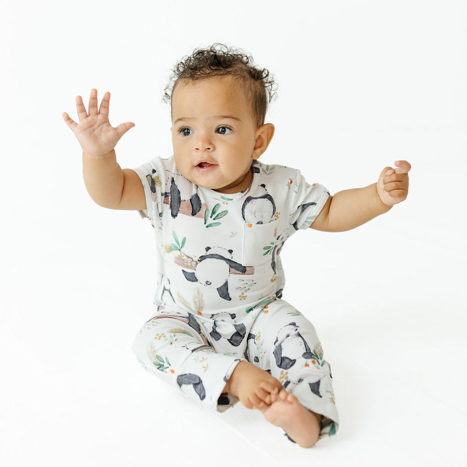 A baby sitting on a white studio background wearing a short-sleeve pajama romper and matching pants with a penguin print.