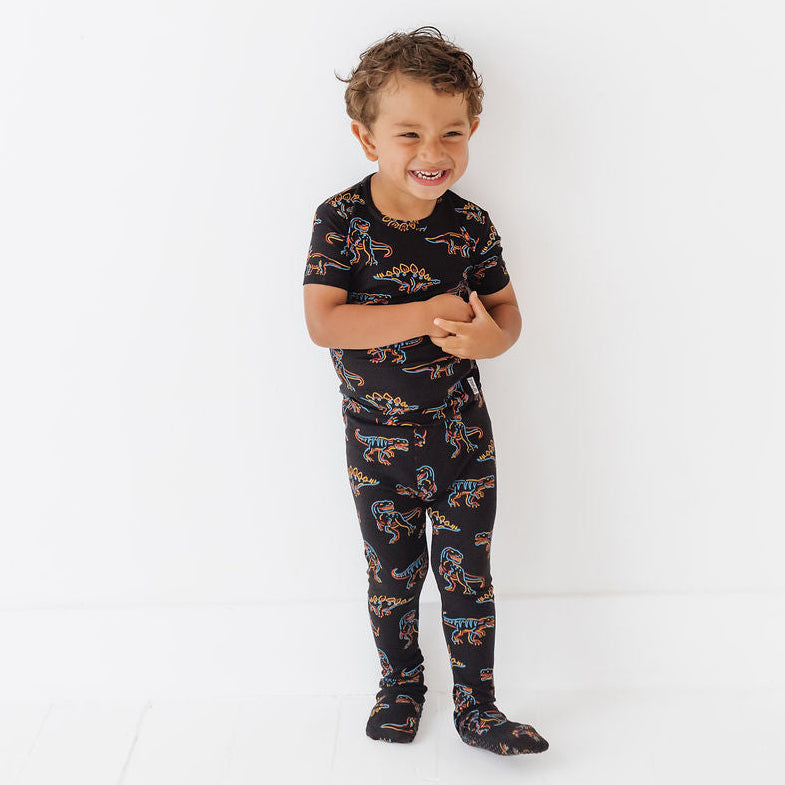 Child wearing a black pajama set with dinosaur print on a white background