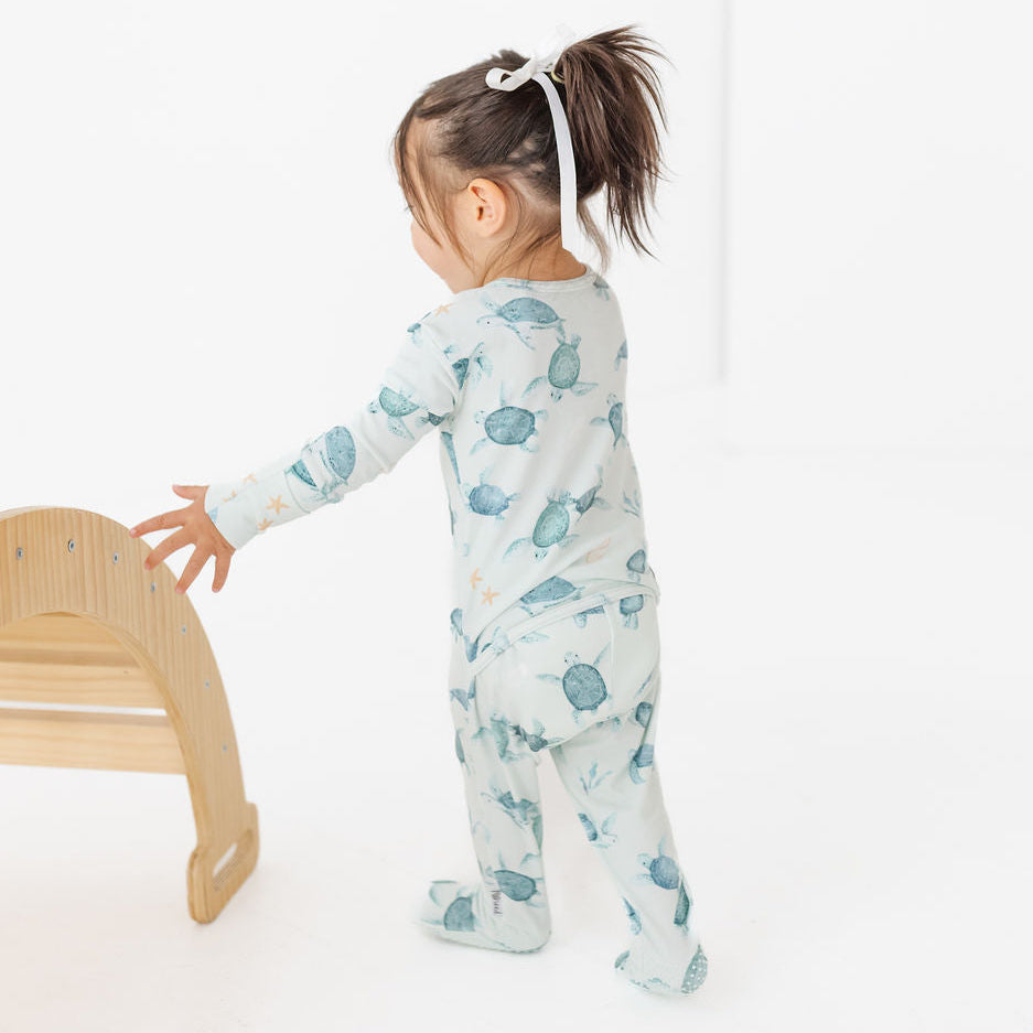 Child wearing a blue and white onesie with a pattern, standing on a white background.