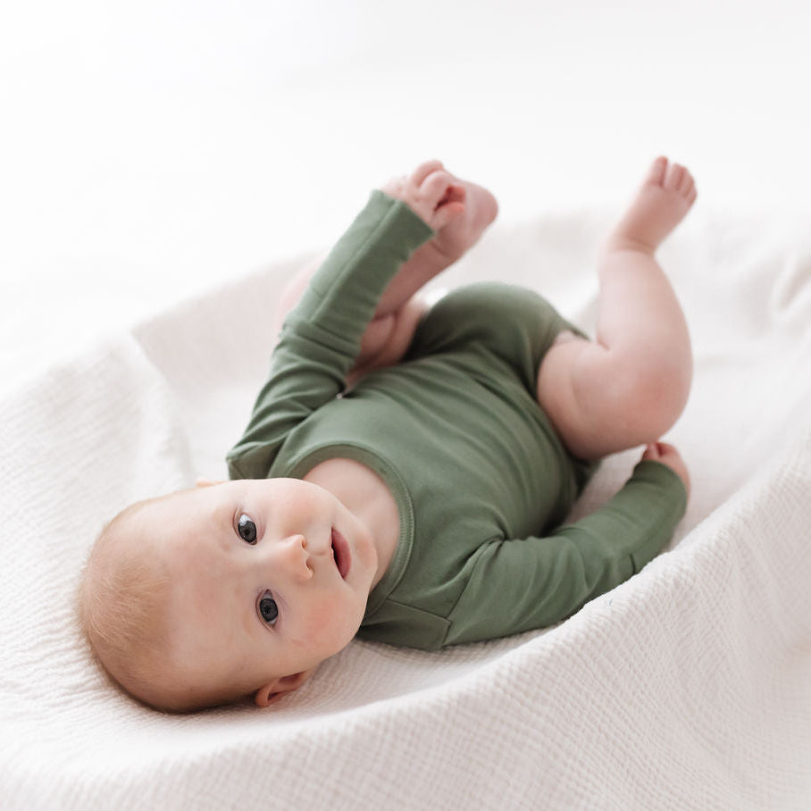 Baby in a green onesie lying on a white blanket