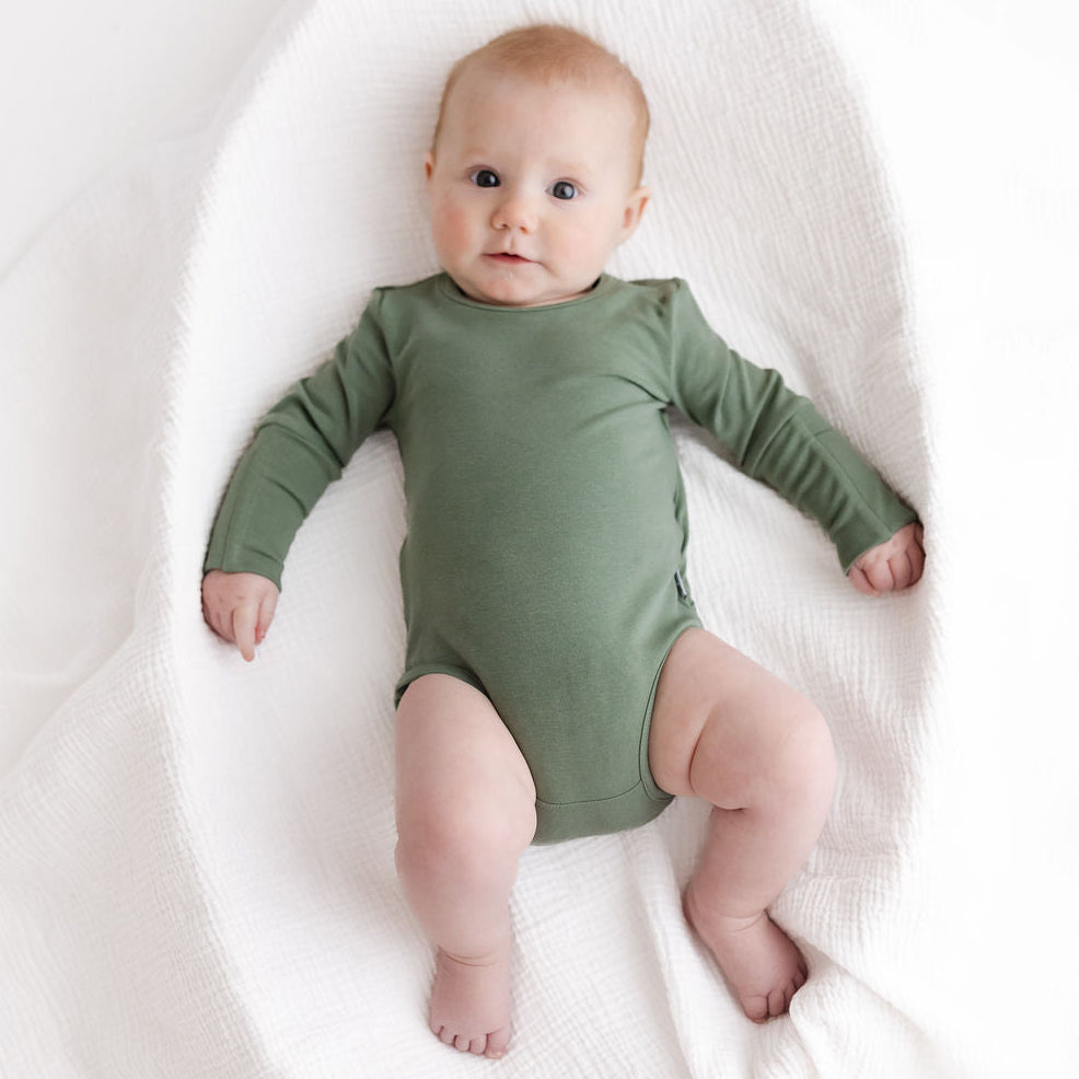 Baby wearing a green onesie lying on a white blanket