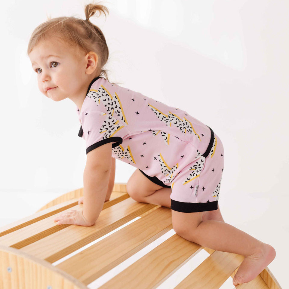 Child wearing a pink outfit with black and yellow patterns on a wooden surface