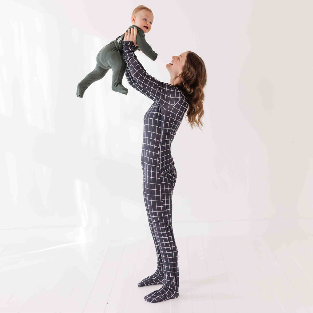 Woman in a black grid-patterned onesie holding a baby against a white background