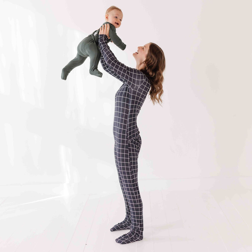 Woman in a black grid-patterned onesie holding a baby against a white background