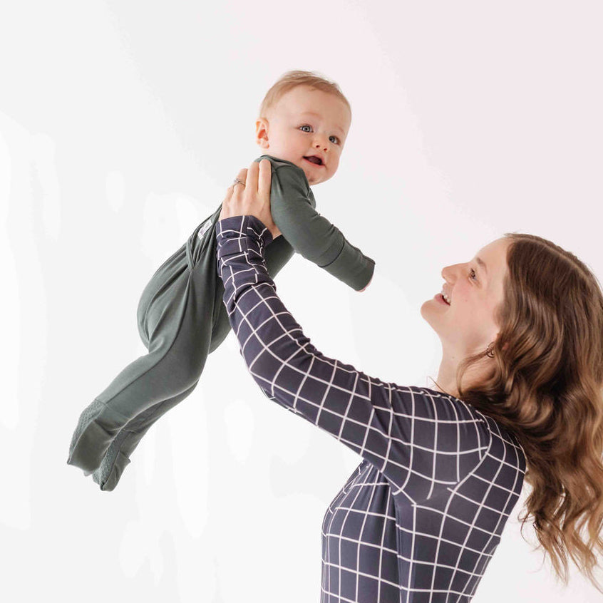 Woman holding a baby wearing a green outfit against a white background