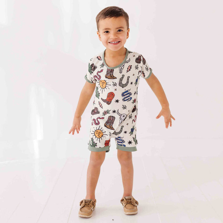 Child wearing a romper with cowboy-themed print on a white background