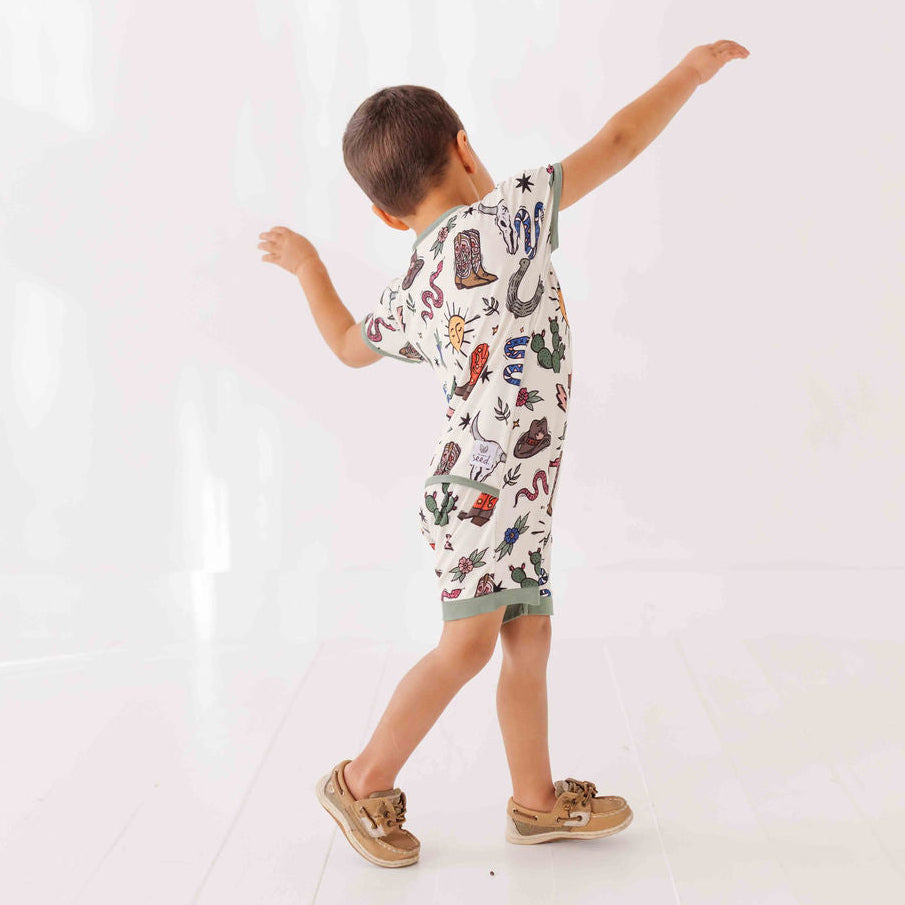 Child wearing a patterned outfit with arms outstretched on a white background