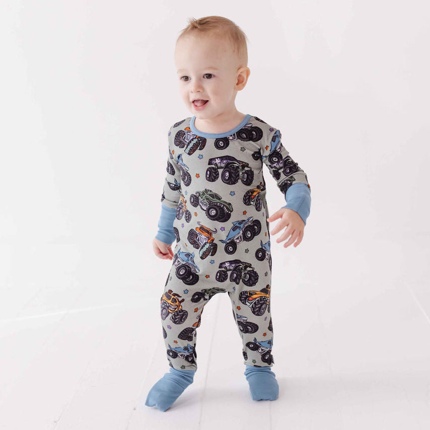 Baby wearing a onesie with monster truck pattern on a white background