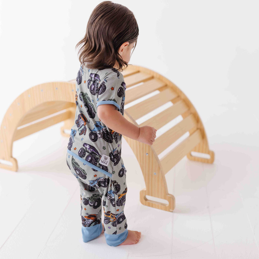 Child in pajamas standing next to a wooden climbing toy on a white floor.