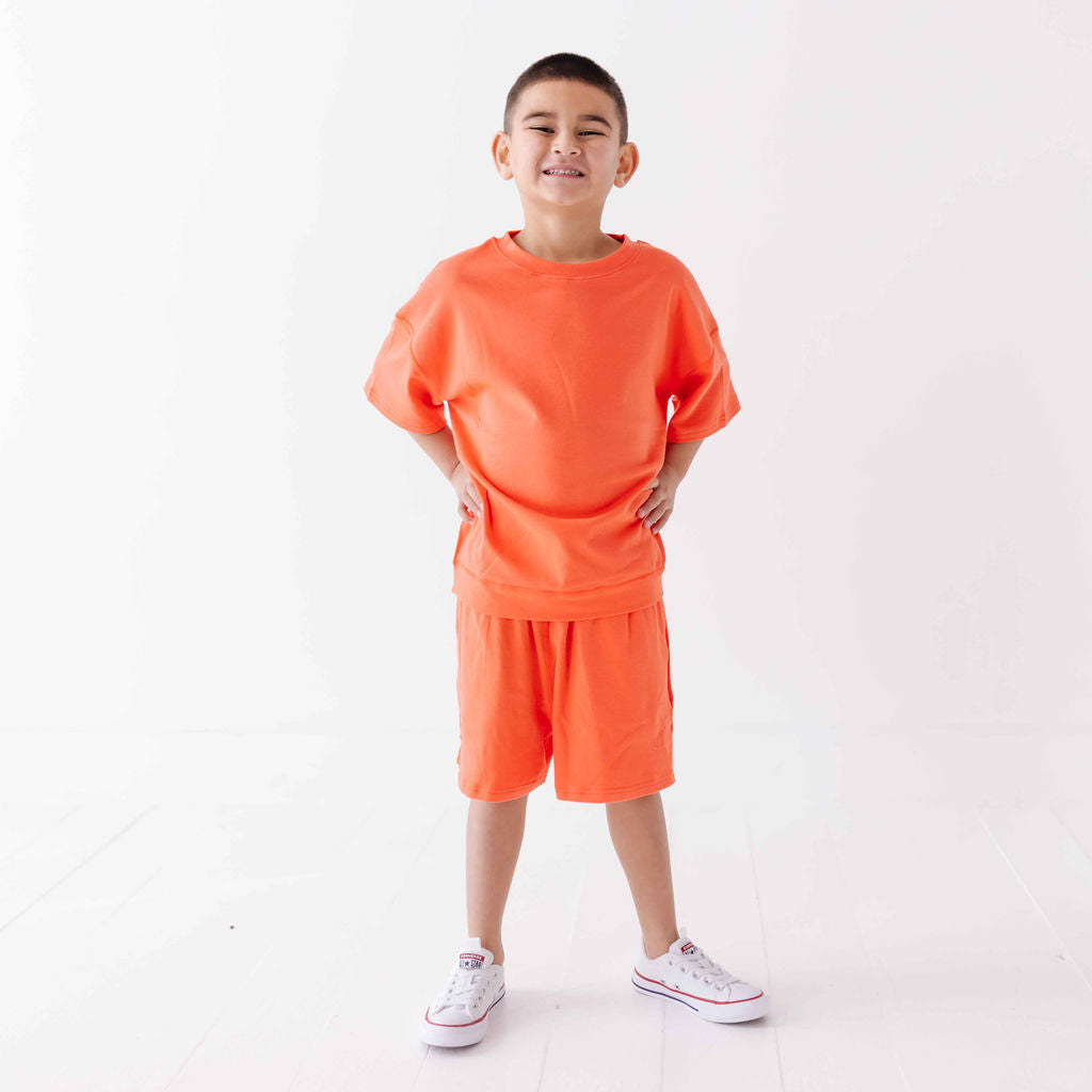 Child wearing an orange outfit with white sneakers on a white background