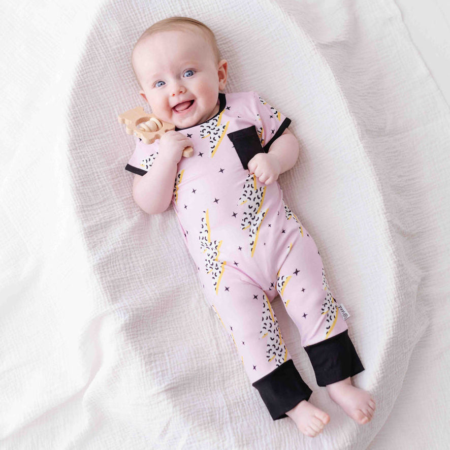 Baby lying on a white blanket wearing a pink outfit with black cuffs and yellow accents.
