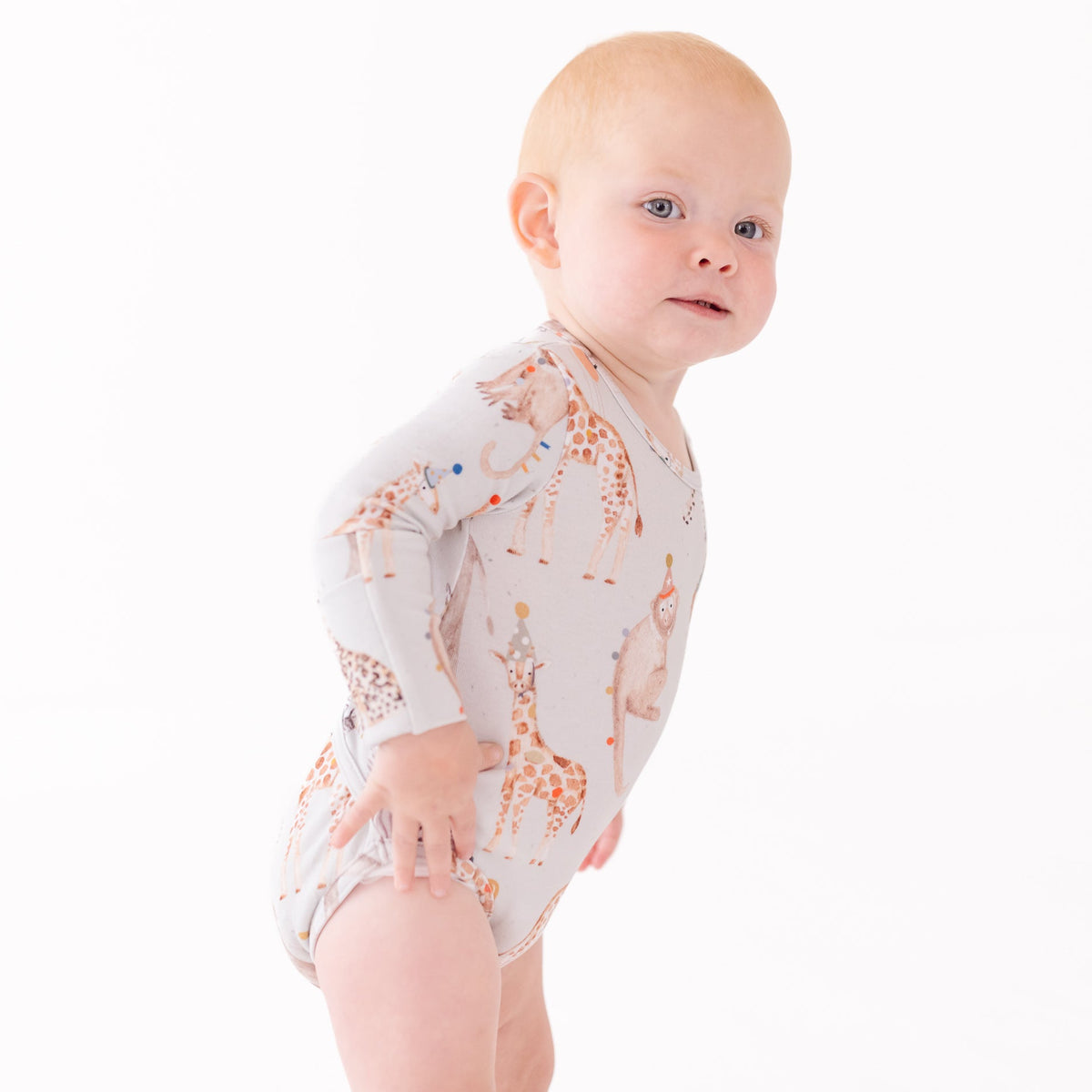 Baby wearing a long-sleeve onesie with giraffe pattern on a white background