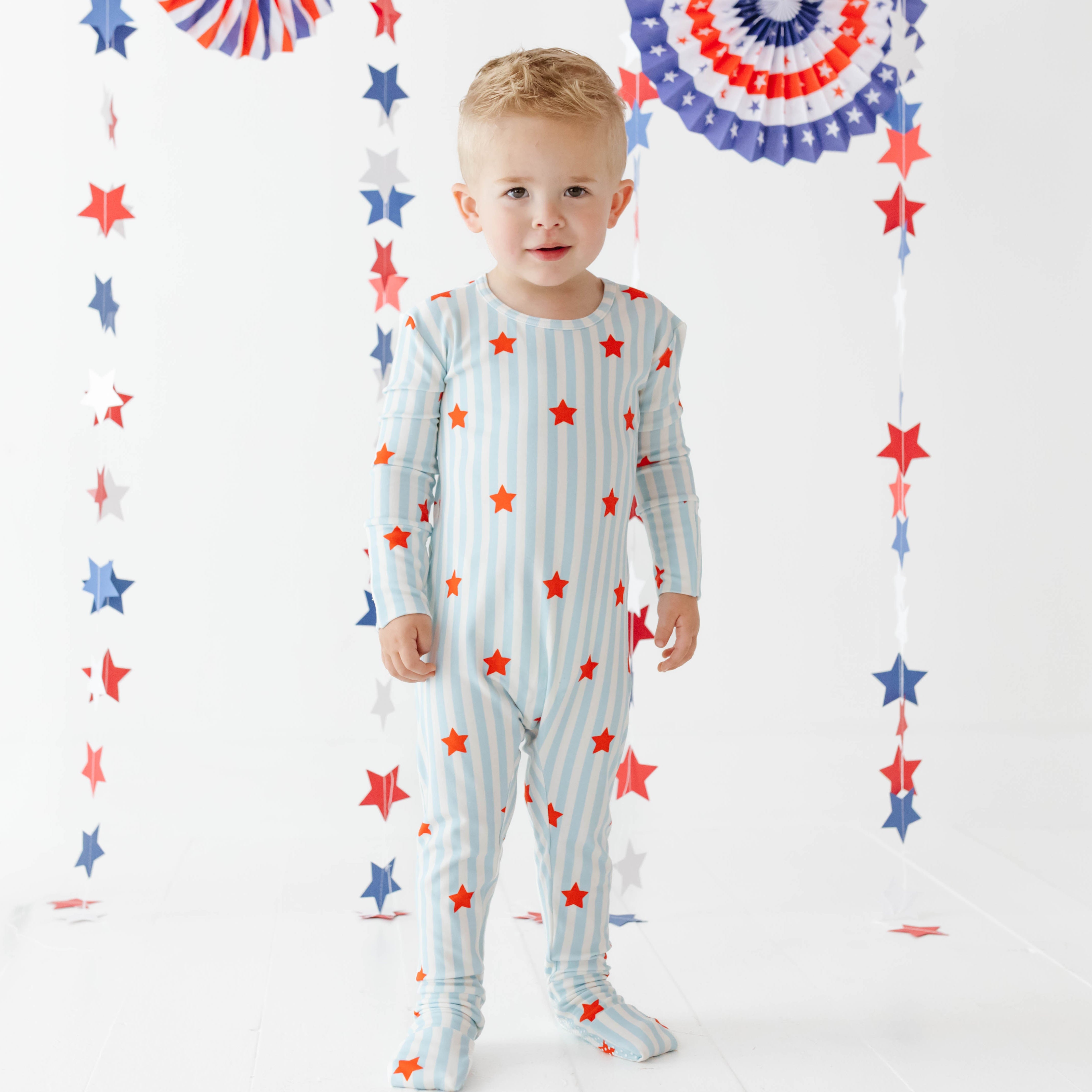 Boy wearing blue and white striped pajamas with red stars and a festive background 