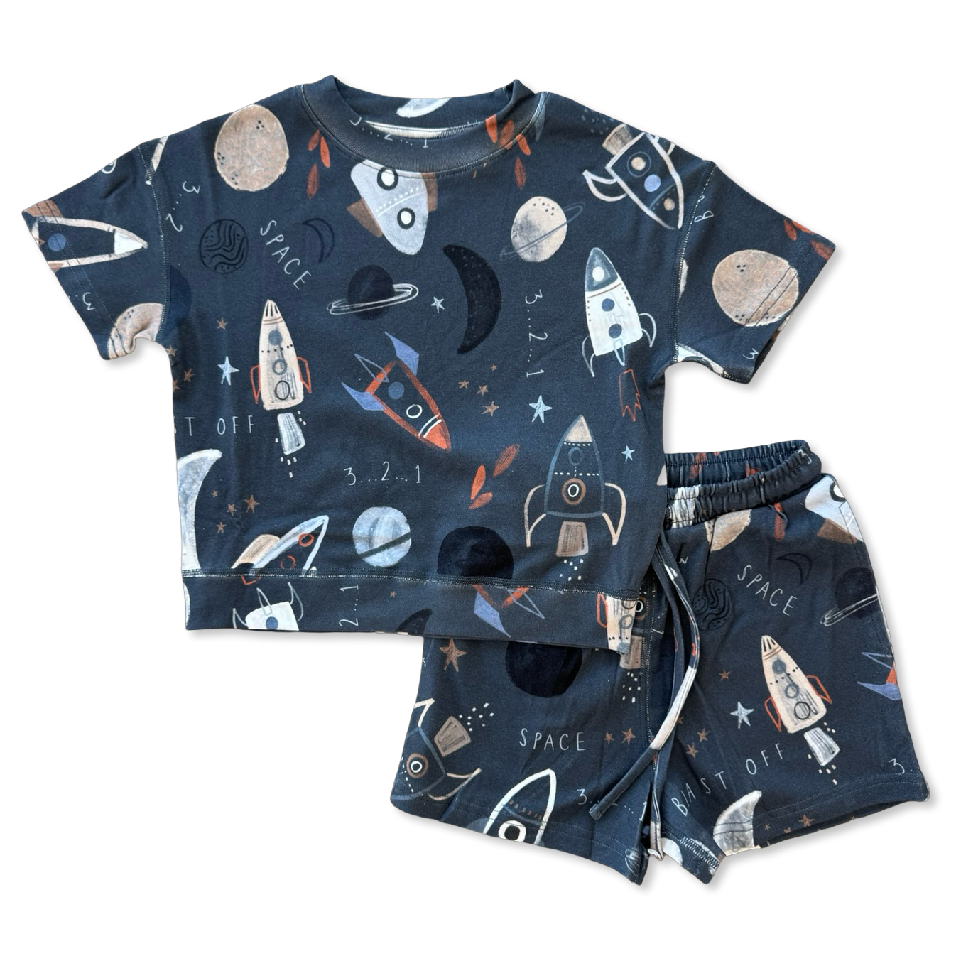 A two-piece kids' pajama set featuring a short-sleeve top and matching shorts in dark navy blue with a playful space-themed print of rockets, planets, moons, stars, and the words 'SPACE' and 'SET OFF'.